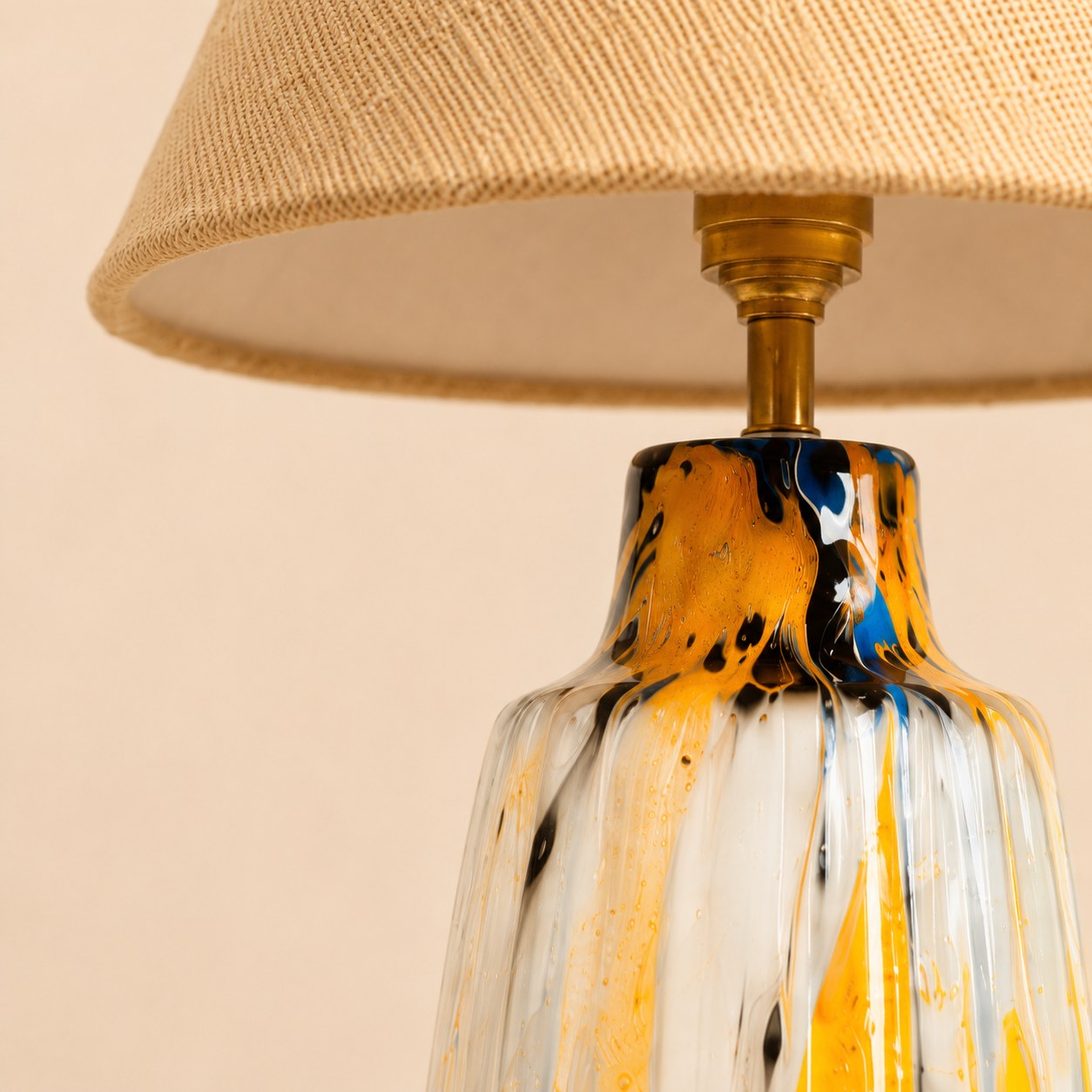 Close-up of textured beige shade, brass-finish neck, and glossy marbled ceramic base